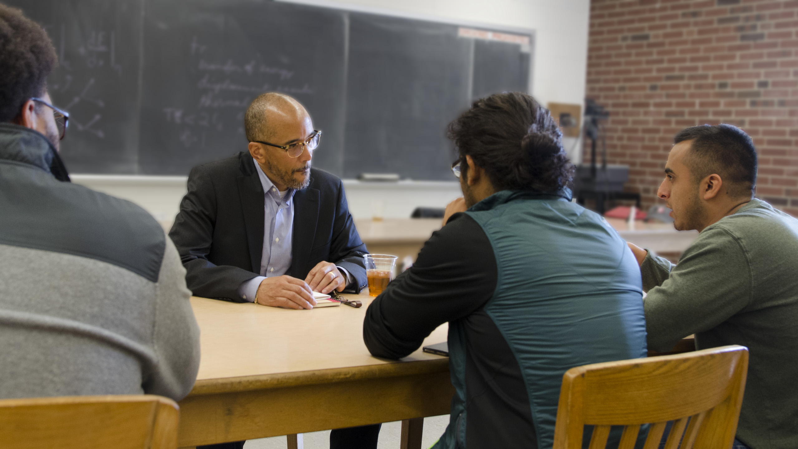 An alum volunteer talking with students at a classroom table