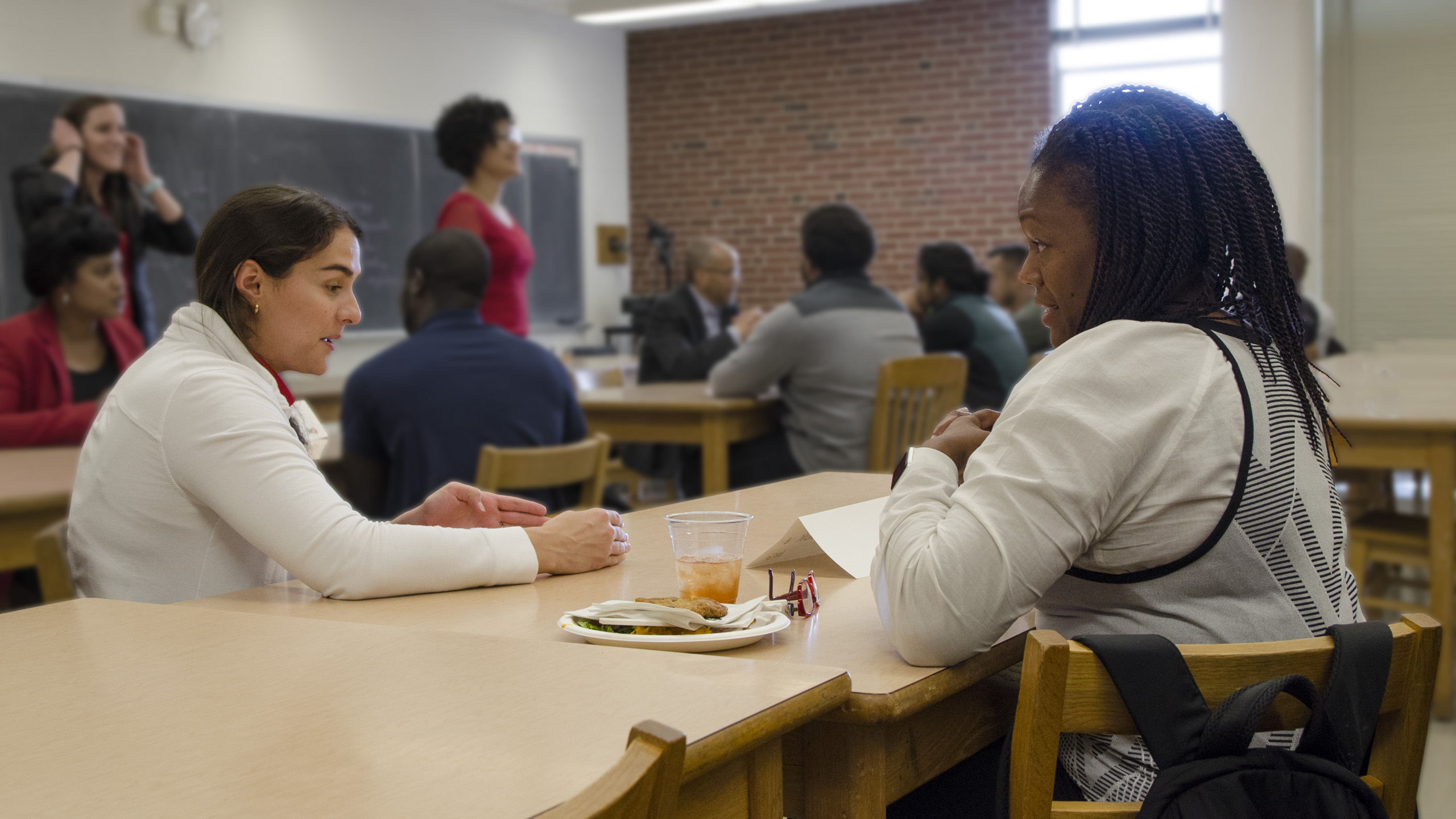 A grad student sitting at a classroom table talking with a prospective student.