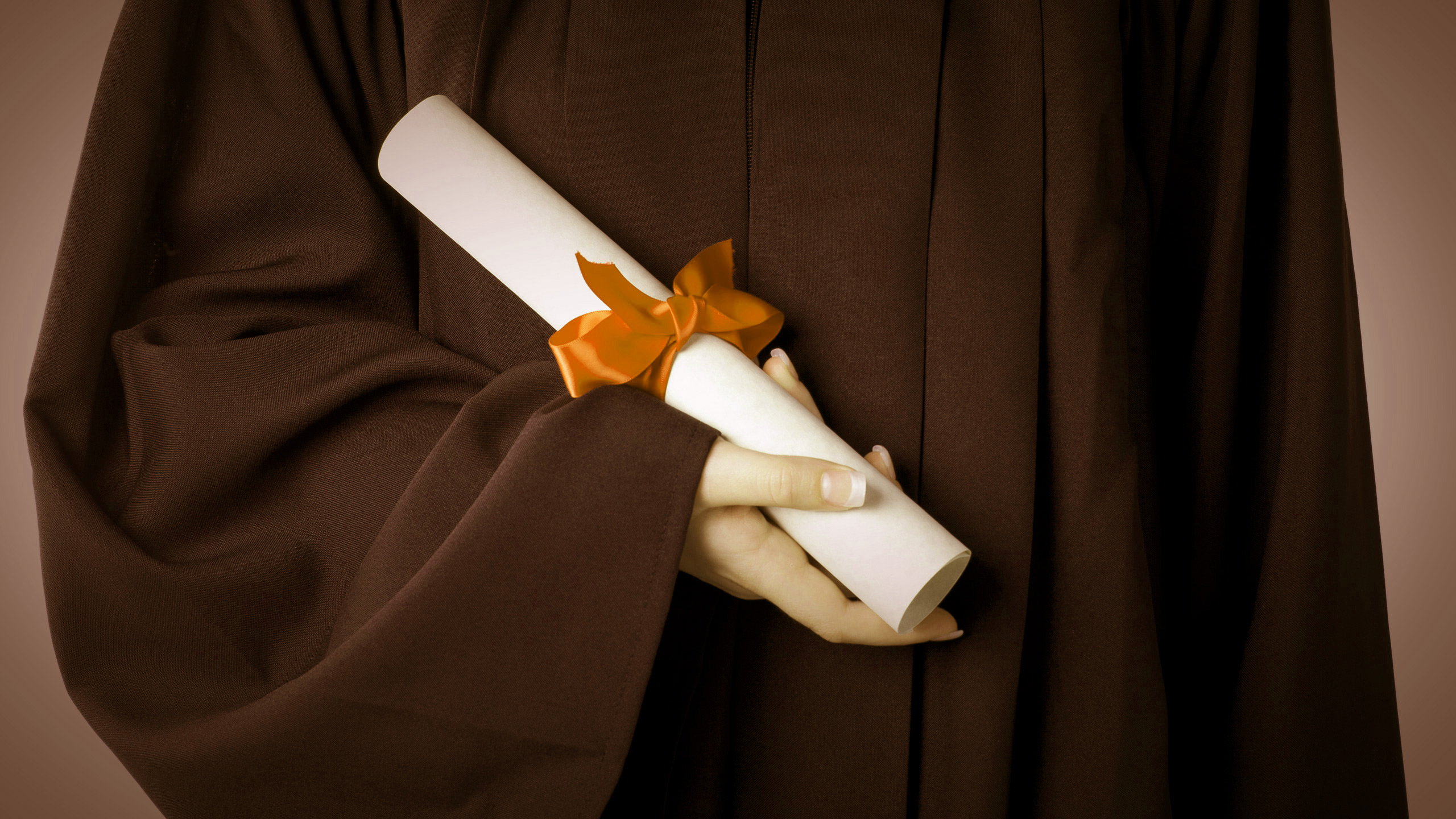 A student in a graduation gown holding a degree in her hand.