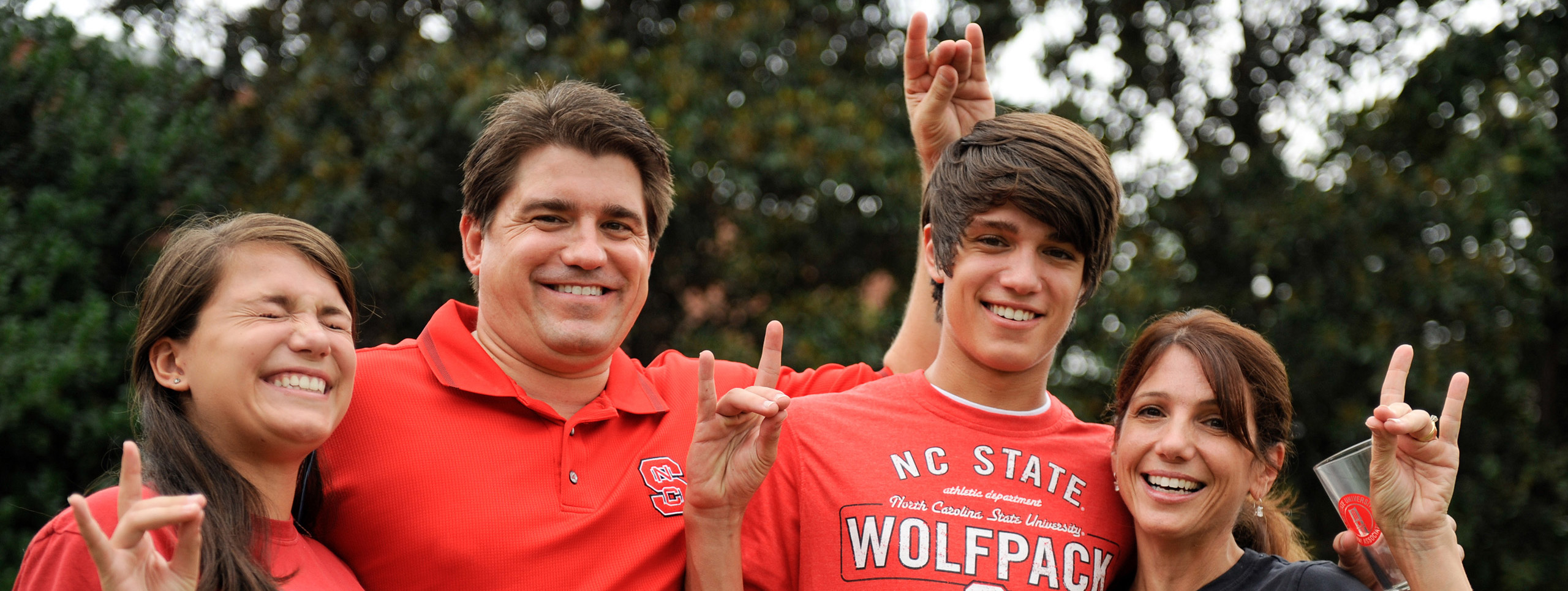 A current NC State student and their family, smiling and throwing wolfies.
