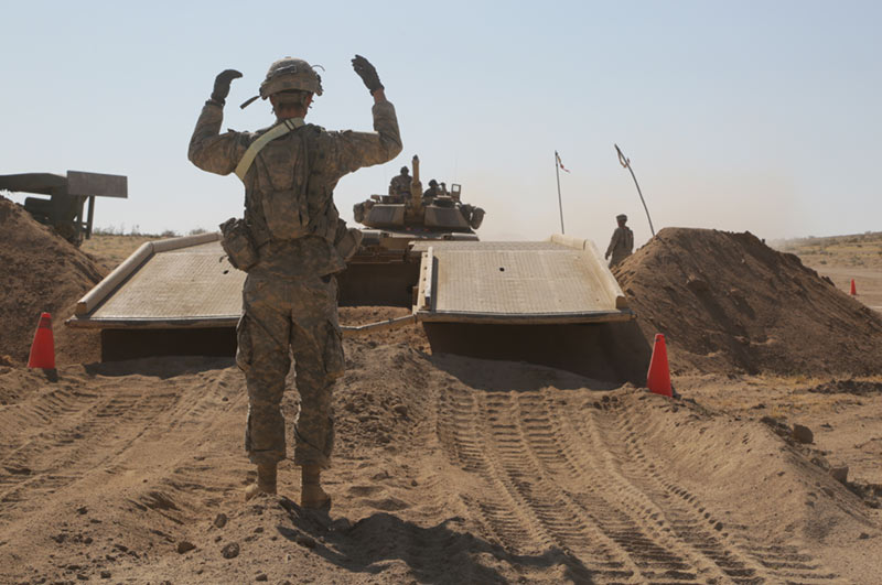 Soldiers guide an M1A1 Abrams tank across a portable bridge at the NTC