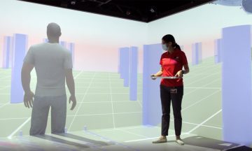 Assistant professor Karen Chen standing in her virtual reality CAVE holding a keyboard