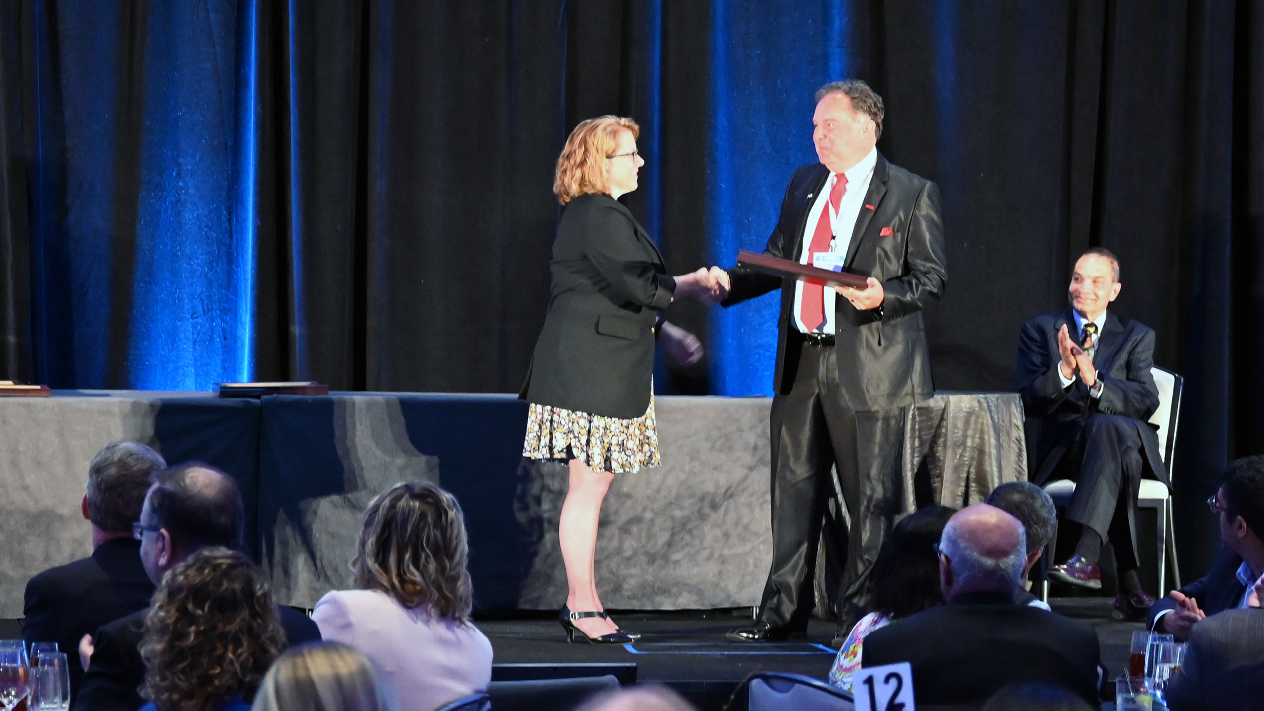 Tony Blevins shakes hands with the IISE president-elect as he receives her Captains of Industry Award