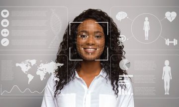 A female standing in front of a gray background having her face scanned and lots of graphics floating around her