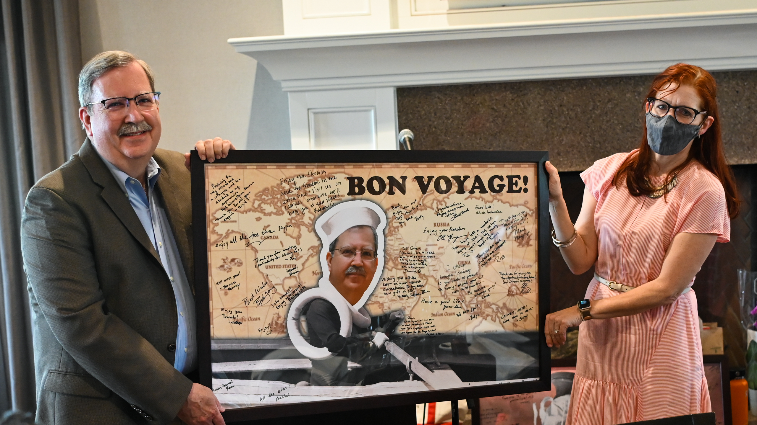 Julie Swann gives Paul Cohen a goodbye poster that says Bon Voyage. The poster is covered with signatures.