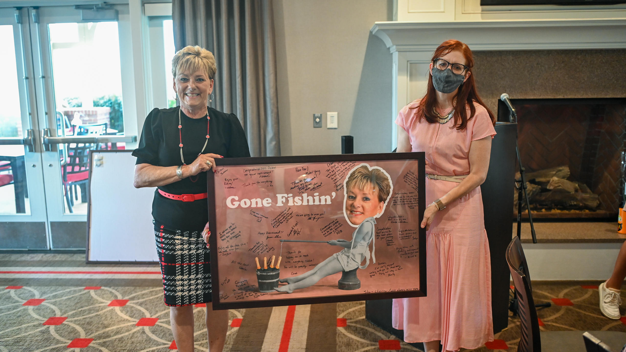 Julie Swann gives Debbie Allgood-Statton  a goodbye poster that says Gone Fishin. The poster is covered with signatures.