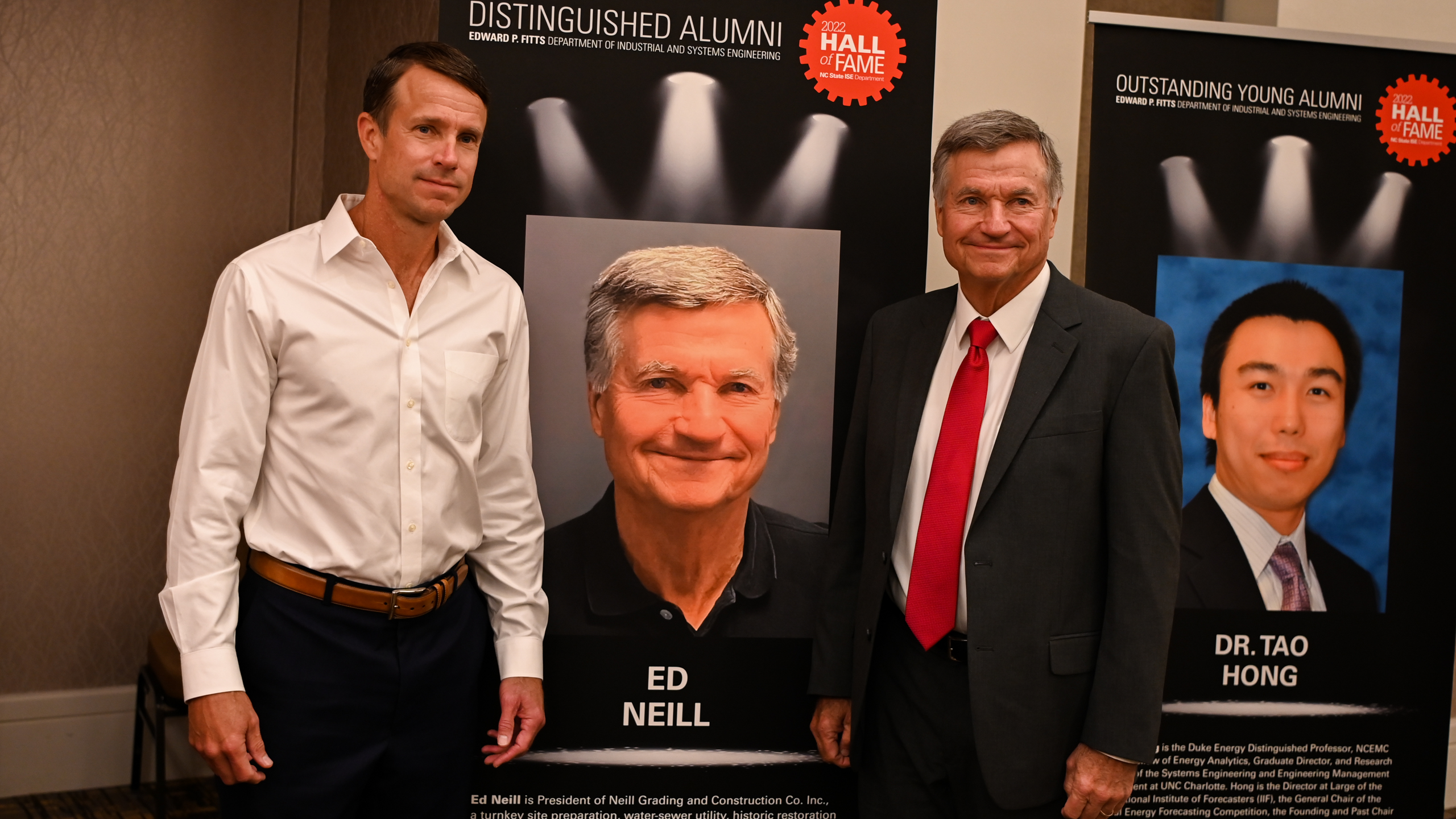 Ed Neill and his son posing in front of Ed's Distinguished Alumni banner
