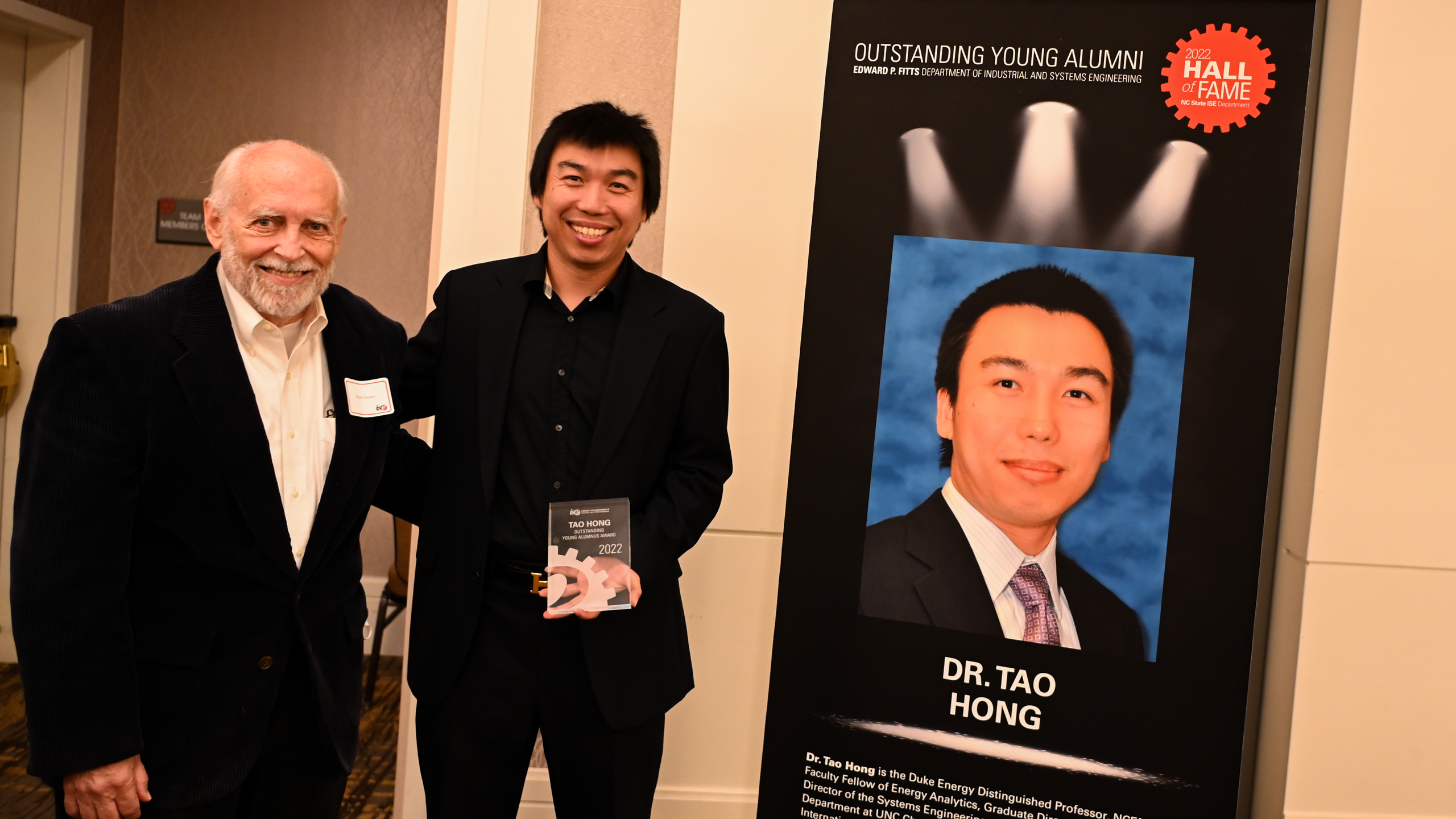 Dr. Tao Hong and one of his professors posing in front of his Outstanding Young Alumni banner