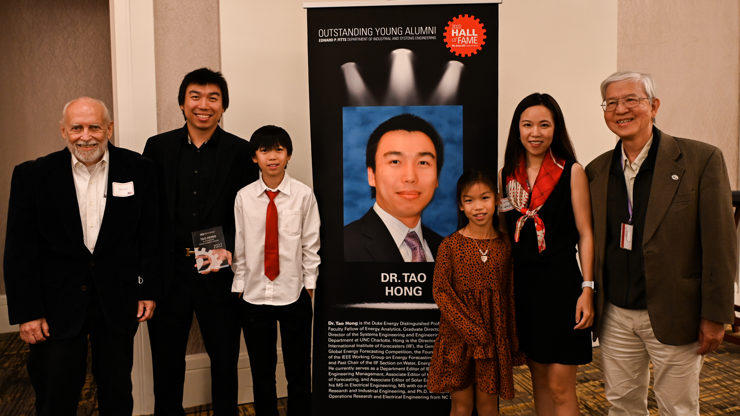 Dr. Tao Hong, his family and friends posing in front of his Outstanding Young Alumni banner