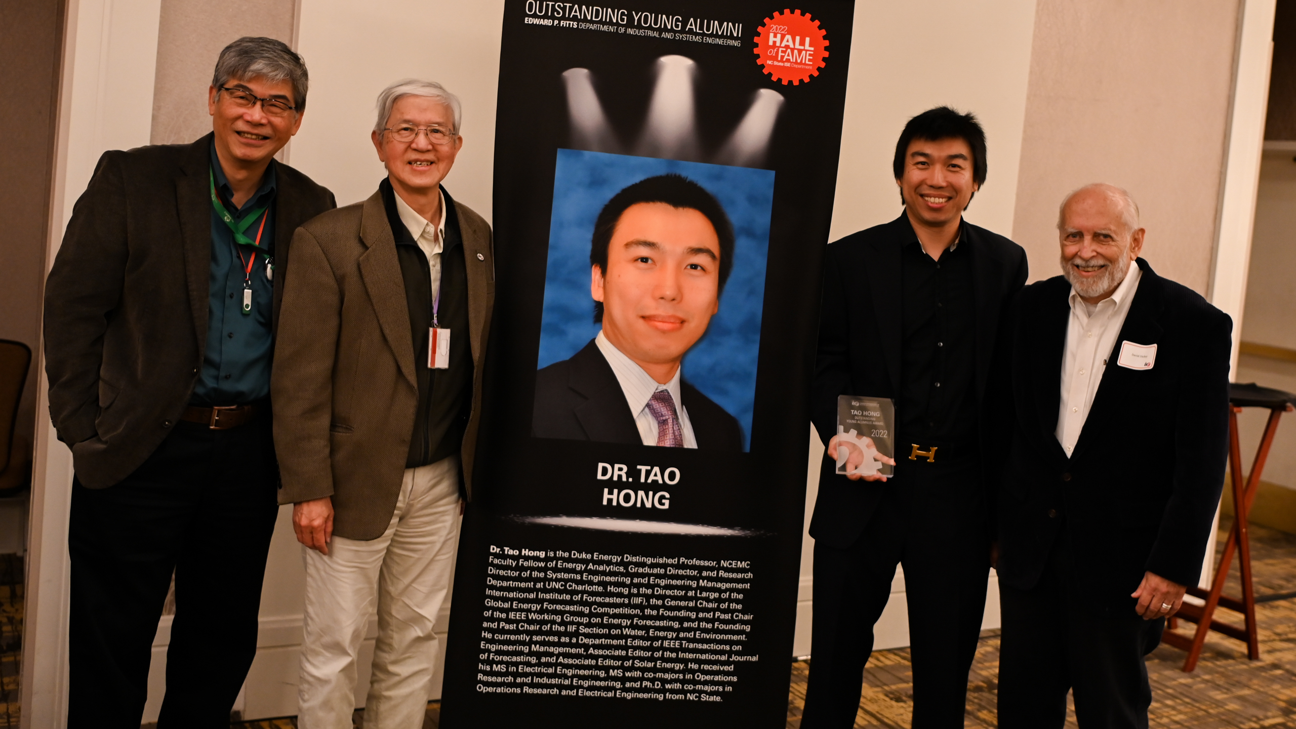 Dr. Tao Hong and faculty members posing in front of his Outstanding Young Alumni banner