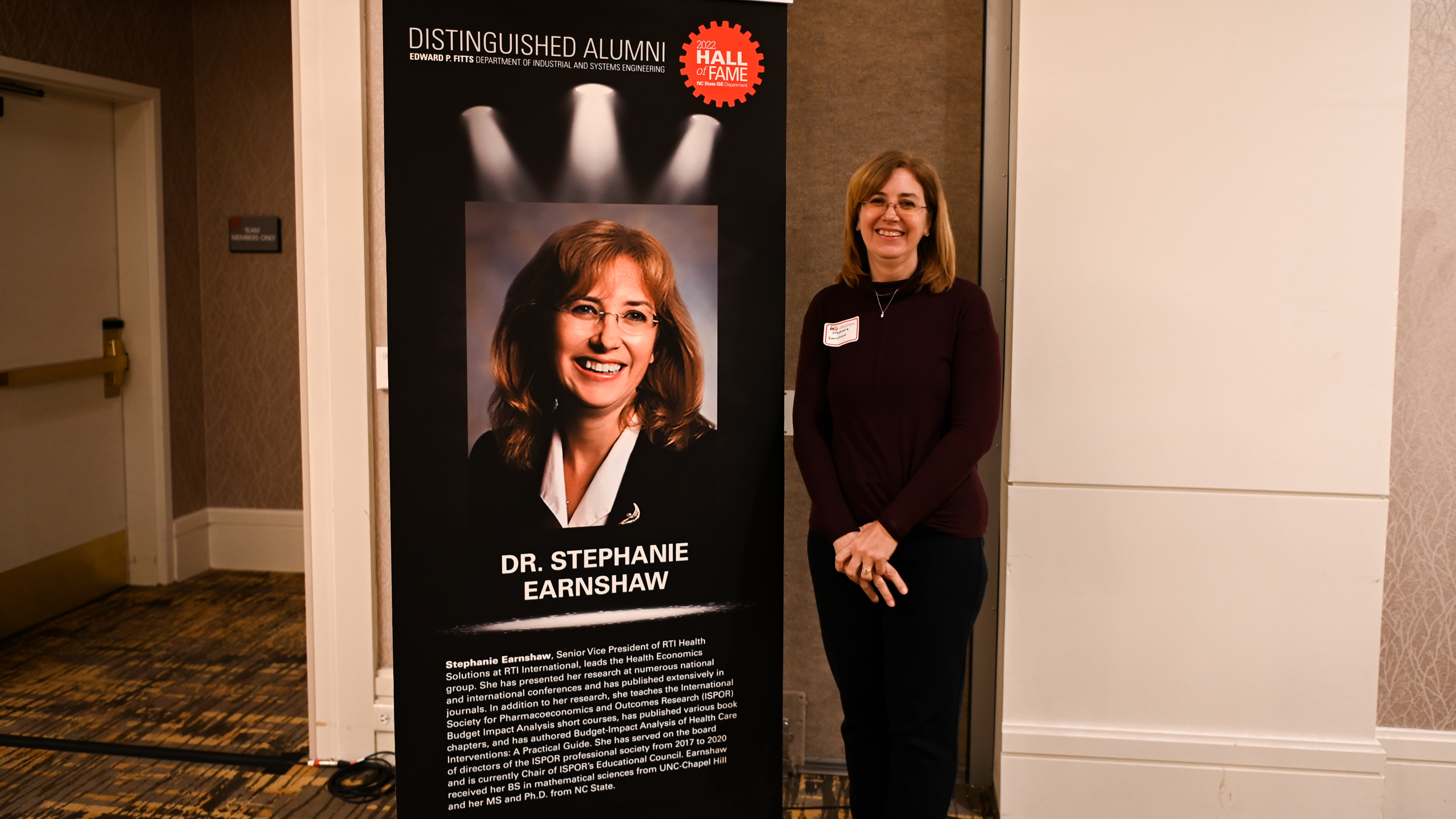 Dr. Stephanie Earnshaw posing in front of her Distinguished Alumni banner