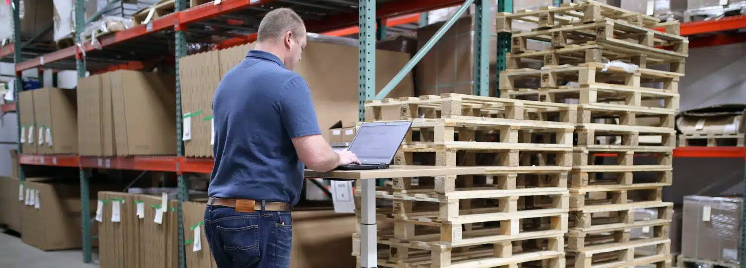 A man standing in a warehouse working on a laptop