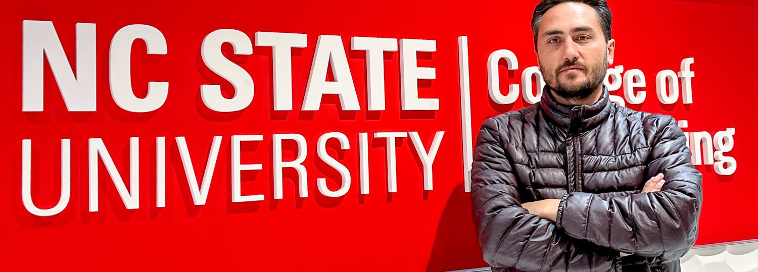 Unal standing in front of a sign that says NC State University