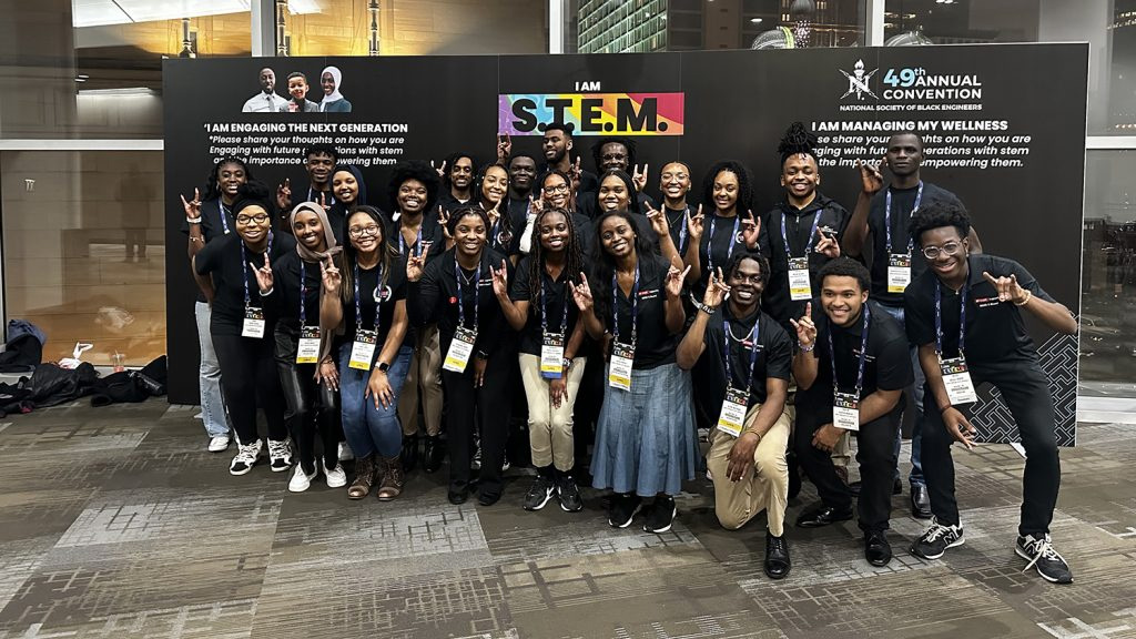 NSBE Convention attendees pose for a group photo in front of an event banner.