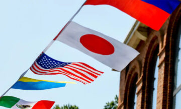 The American and Japanese flags blow in the wind on a line next to a brick building on campus